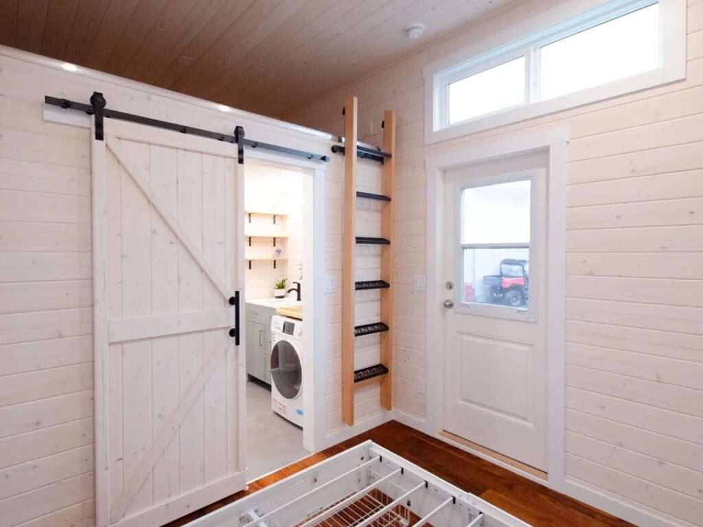 View from the bedroom looking towards a white sliding wooden barn door, a wall-mounted ladder leading to a storage loft, and a glass pane entry door.