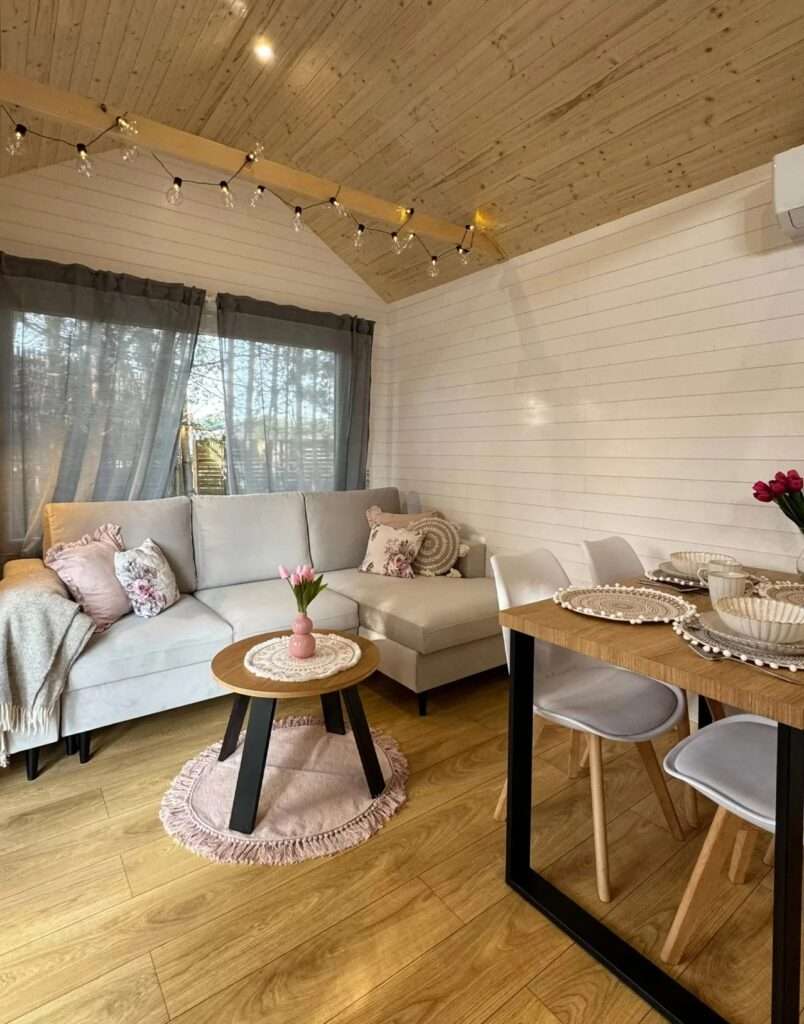 Cozy Scandinavian living room in a tiny house with warm lighting, wood ceiling, and comfortable seating.