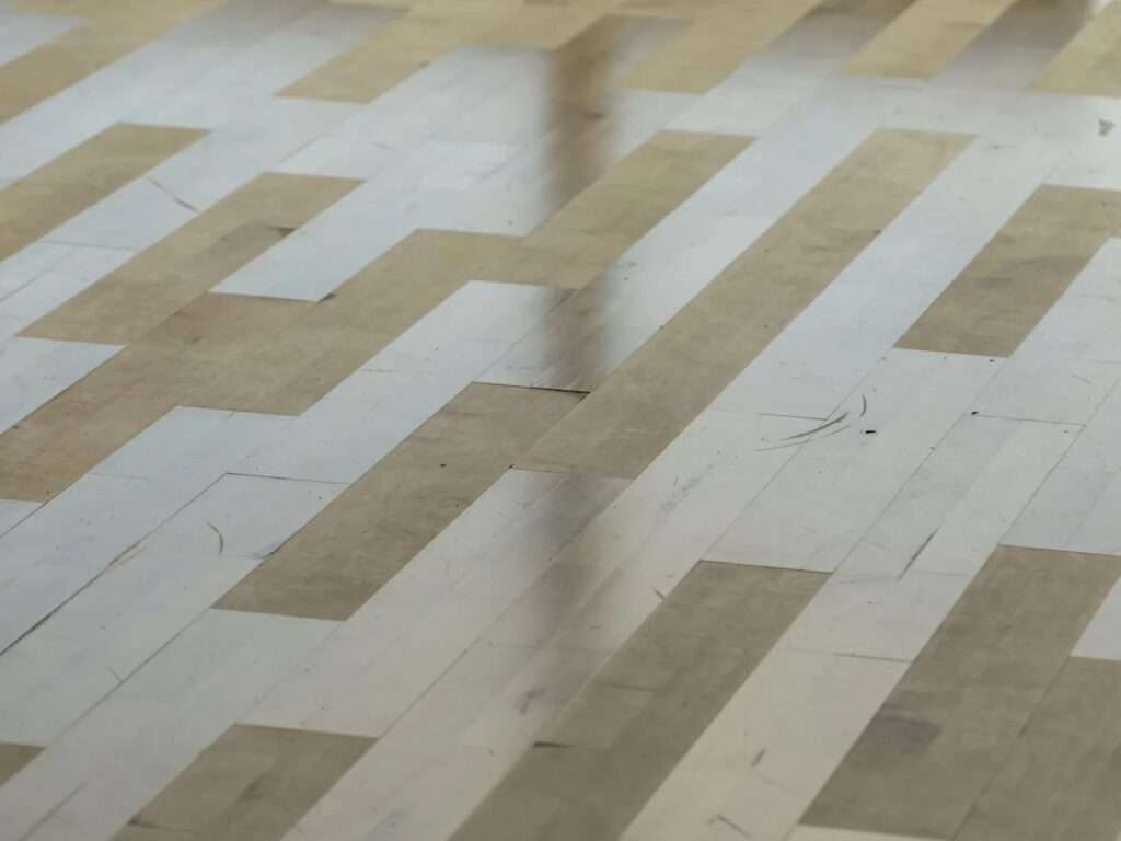 Close-up detail of recycled wooden parquet flooring inside the TRAE project showing natural variations and light scratches from reclaimed timber.