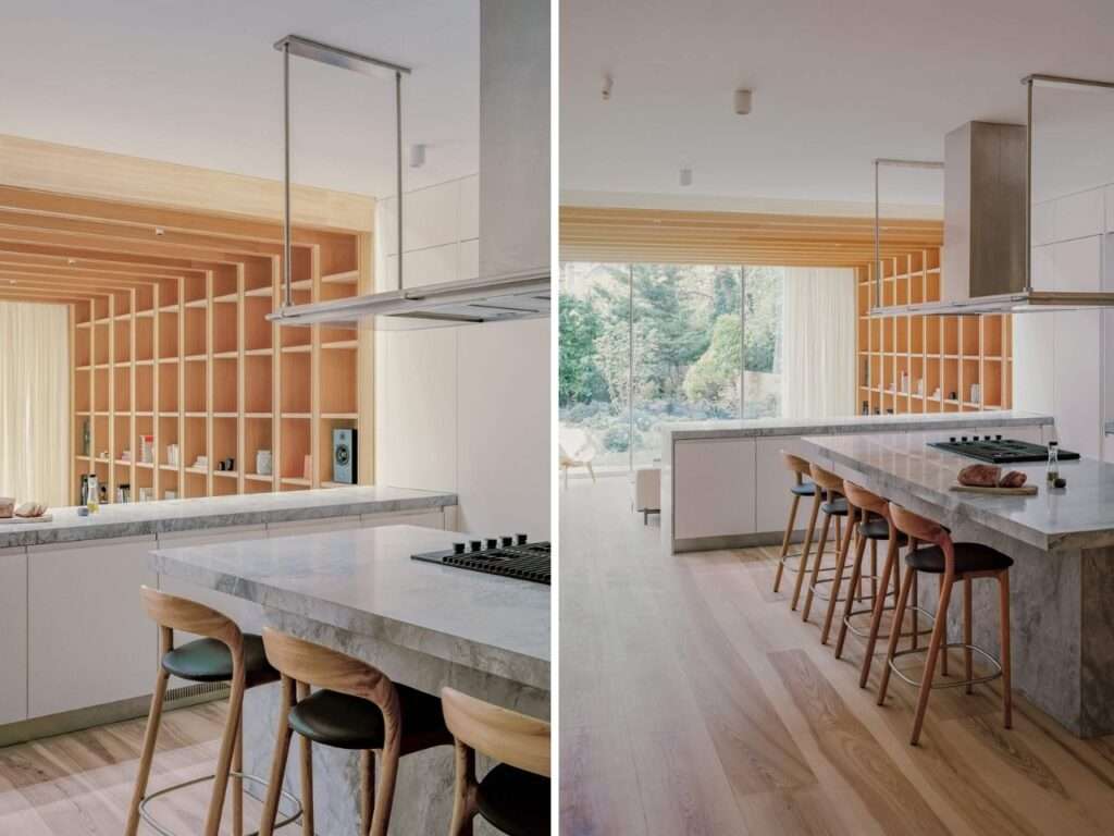 Split view of a modern kitchen featuring a Bianco Eclipse quartzite island countertop overlooking a lowered timber-lined living space.