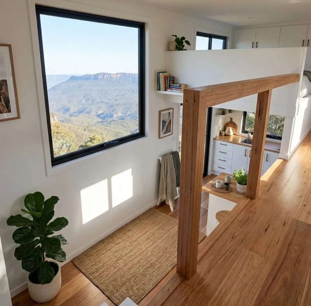 Interior view looking down from a wooden loft walkway next to a massive panoramic window overlooking distant mountains.