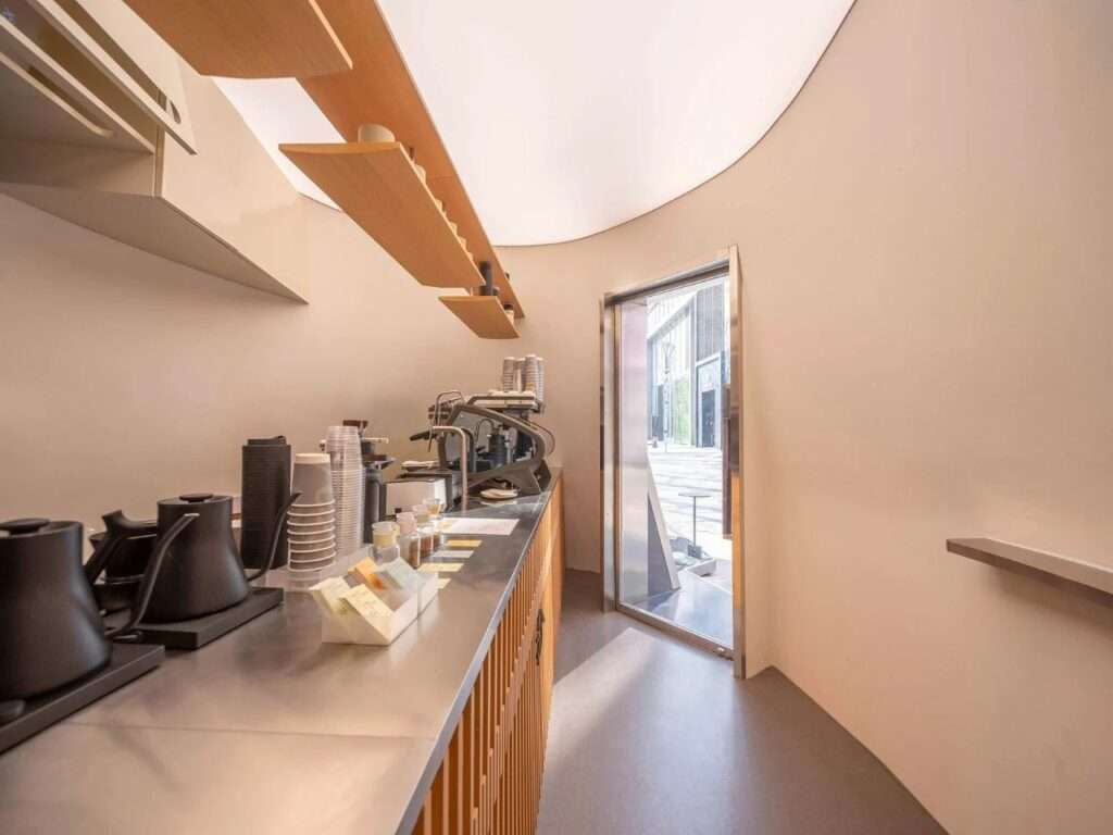 Interior view of the linear brewing counter inside the Kurasu coffee pavilion, showing espresso equipment, pour-over kettles, and timber slatted bar.