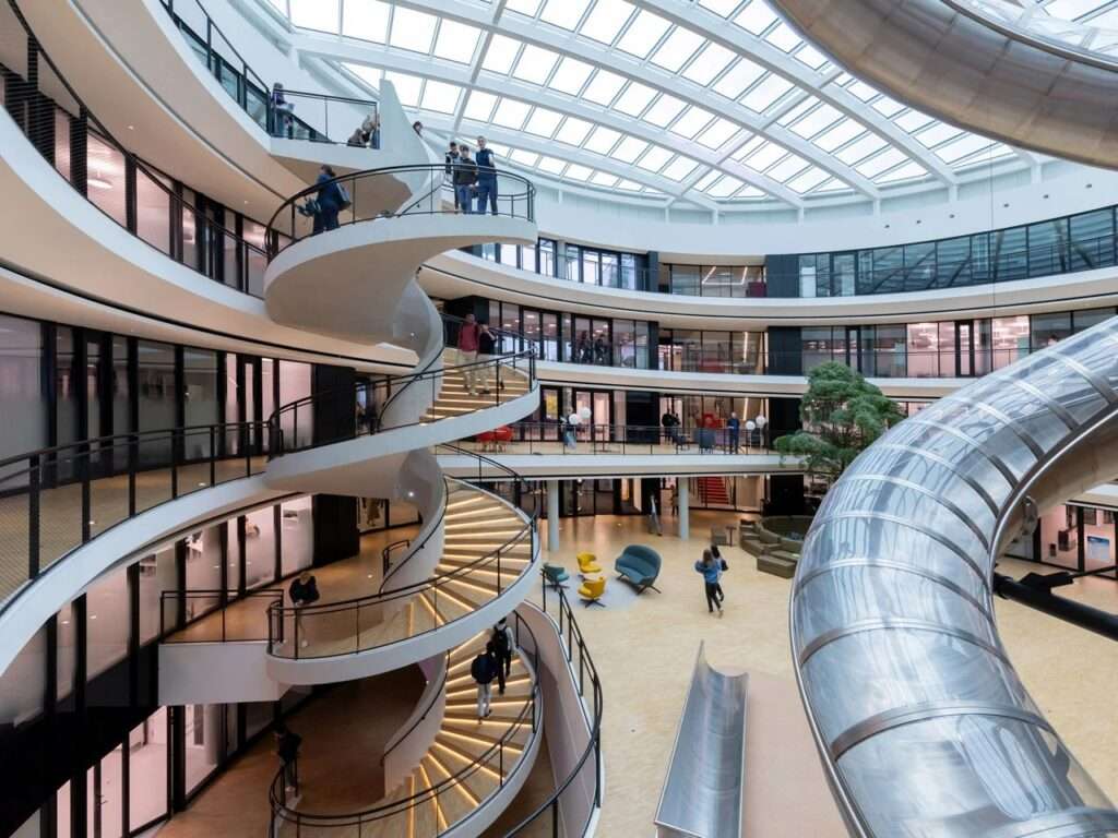 High-angle view of the central courtyard inside the Philo Center showing students walking down an illuminated white spiral staircase adjacent to a curved slide.
