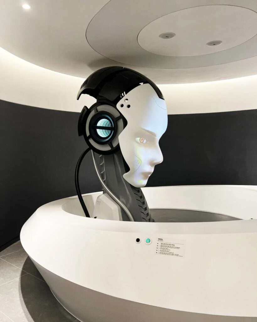 A futuristic white and black humanoid robot head interface inside a circular white pod within the Seoul Robot and AI Museum.