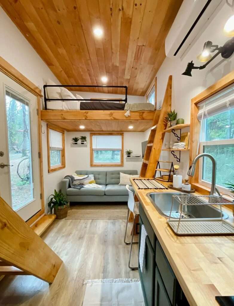 Full interior view of Rasa tiny home looking towards the living room with a grey sofa and multiple windows for natural light.