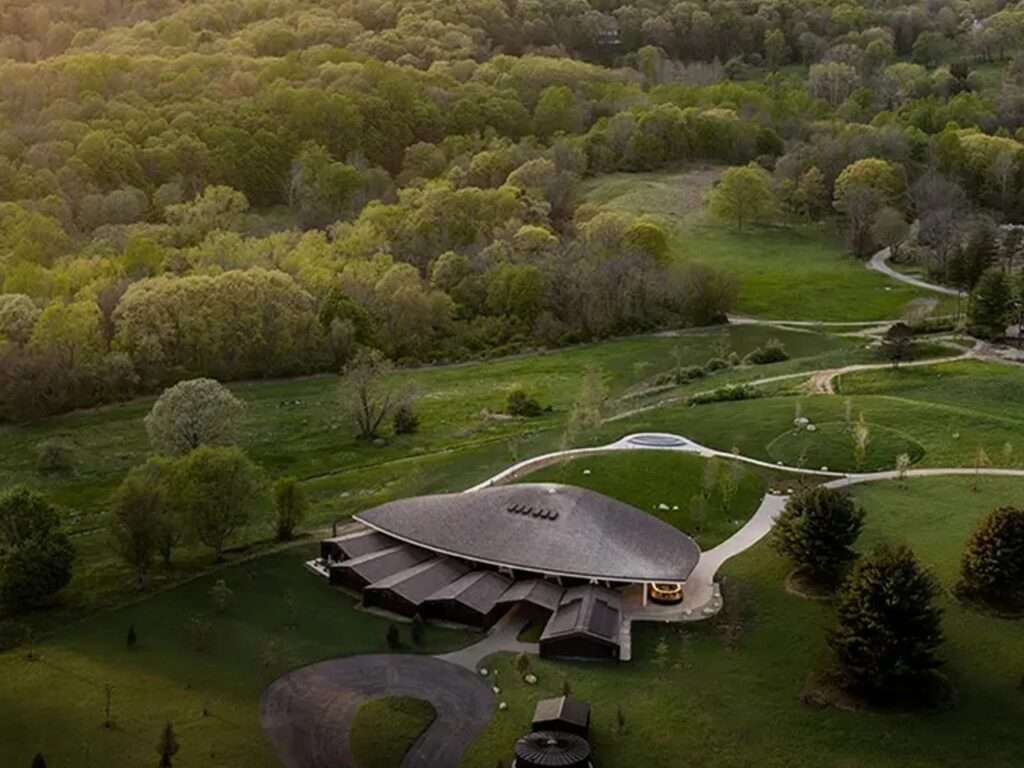 High aerial view of the Studio Gang designed theater complex surrounded by vast green forests and meadows in Garrison, New York.