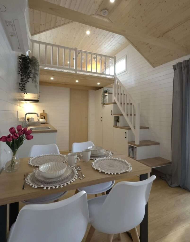 White wooden stairs with integrated storage leading to a sleeping loft in a modern tiny house.