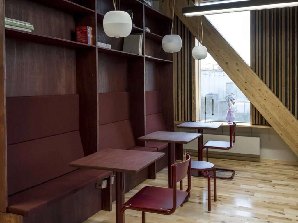 Cafe seating area inside TRAE tower featuring deep red built-in wooden booths, minimalist furniture, and an angled glulam perimeter brace.