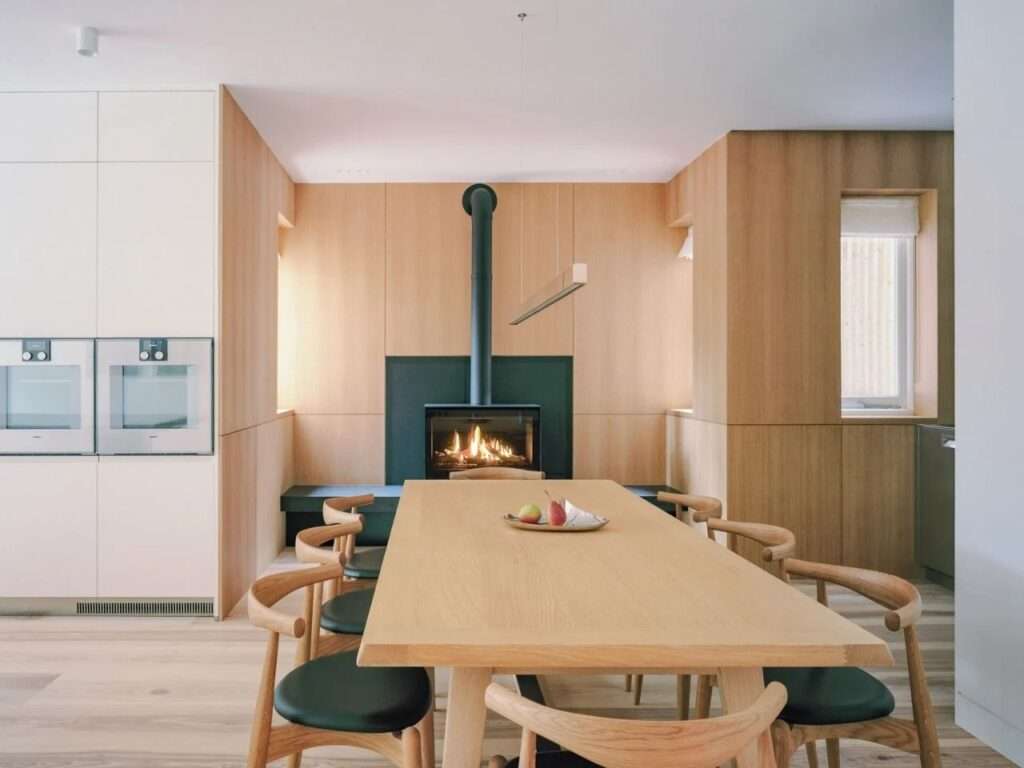 Intimate dining room area with a light wood dining table, matching chairs, and a minimalist black wood-burning fireplace insert.