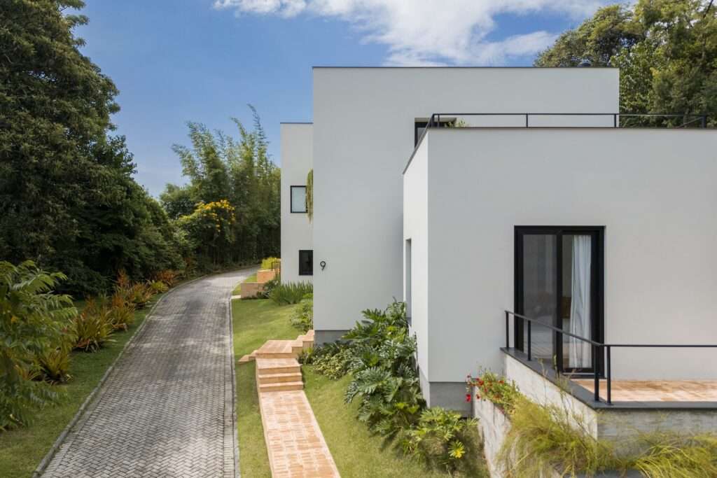 High-angle view of a paved stone driveway running parallel to fragmented white architectural blocks and lush green slopes.