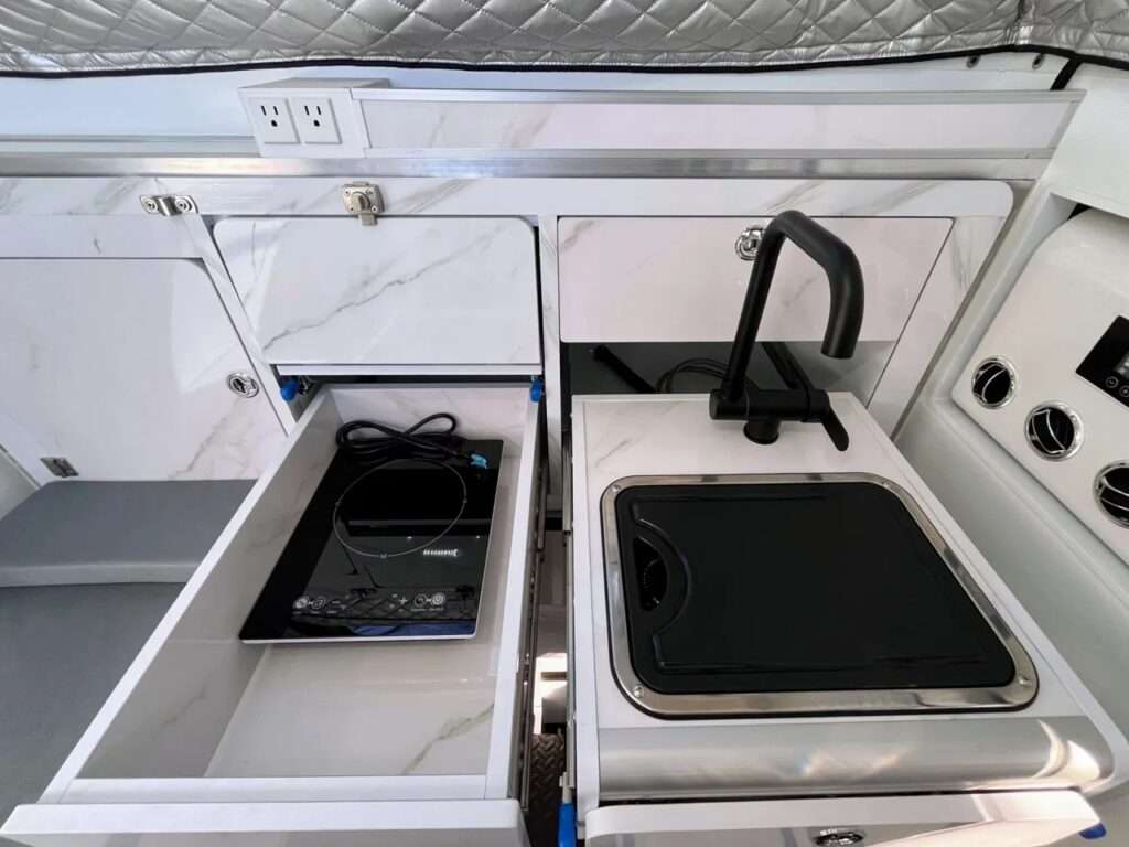 Top-down view of the sliding kitchen modules including the sink and induction stove on a white surface.