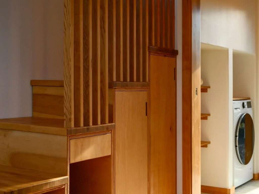 Close-up of custom wood storage stairs with integrated cabinets alongside a laundry niche housing a front-load washer-dryer unit.