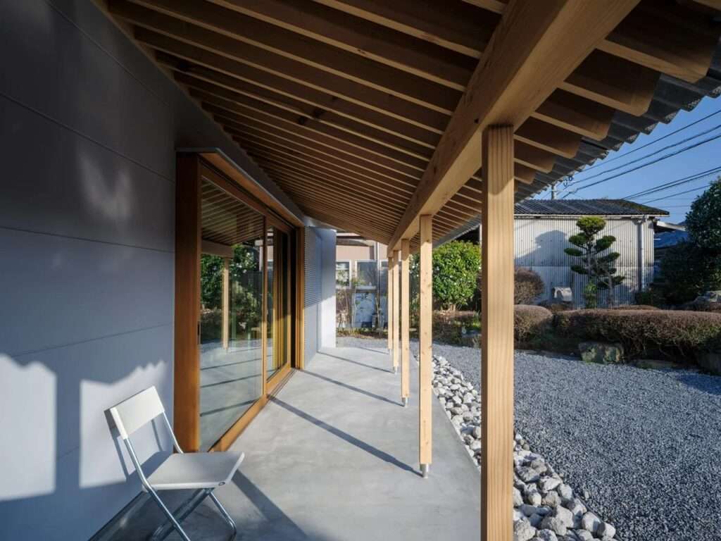 An updated modern Engawa veranda with a concrete floor, wooden structural pillars, an angled timber roof, and a single white folding chair.