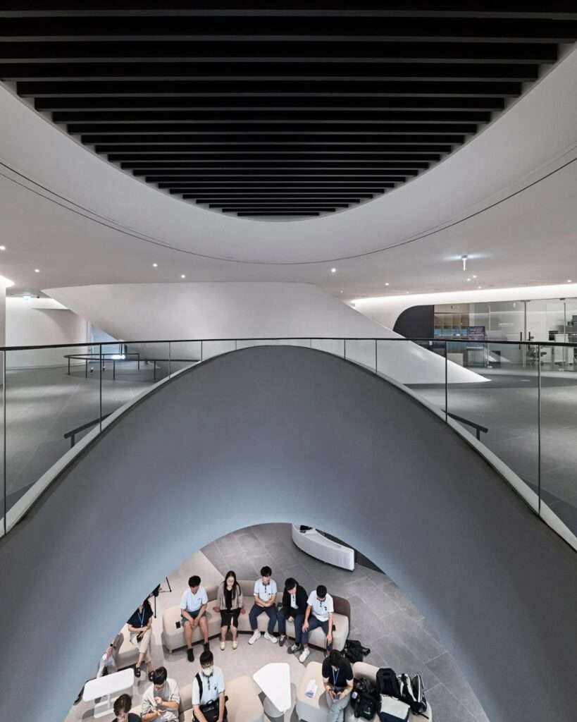 Looking down into a curved vertical atrium void where visitors are seated in a lounge area on the lower floor of RAIM.