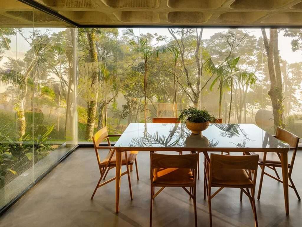 A wooden dining table reflecting the forest view through a large glass window, creating a transparent dining experience.
