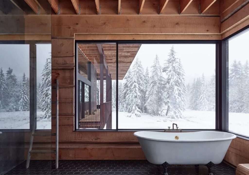 Classic clawfoot bathtub in the Daisy House bathroom, positioned in front of a large corner window overlooking a snowy forest.