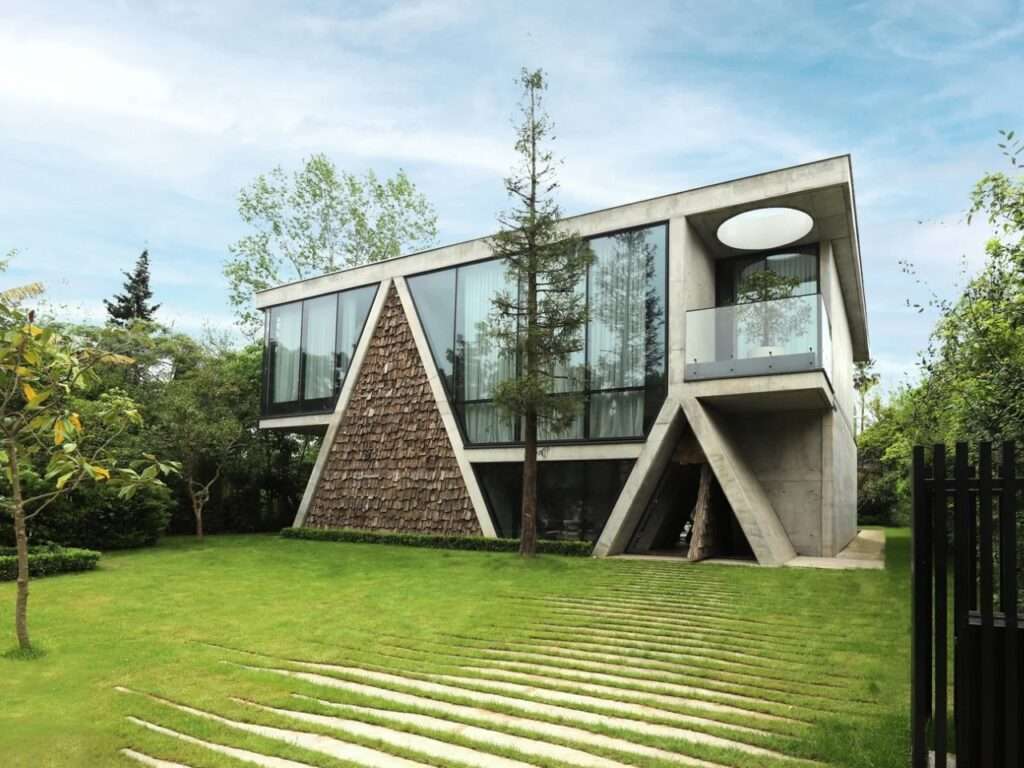 Wide-angle exterior shot of Gable Villa surrounded by a lush green lawn, trees, and a clear blue sky.