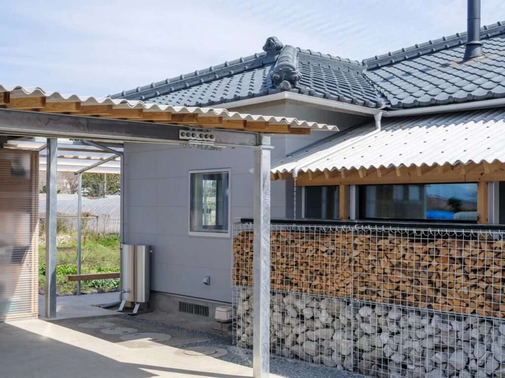 Architectural detail showing the intersection of a historic gray-tiled Japanese roof with a newly installed corrugated metal awning and galvanized steel pillars.
