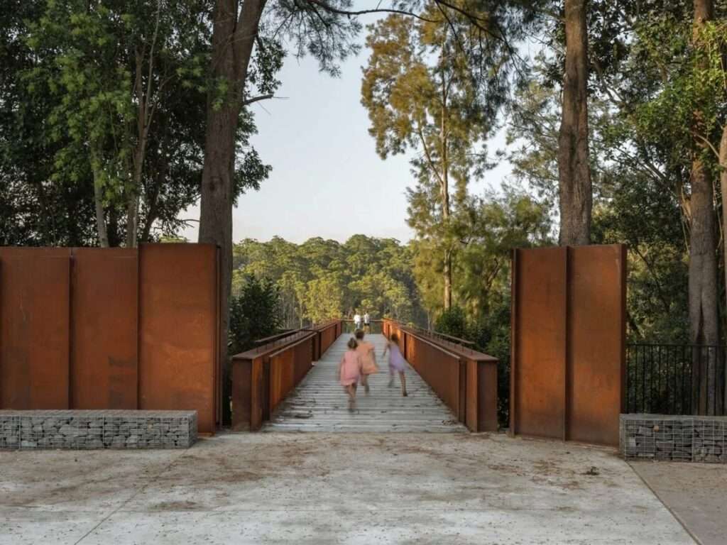 Children running towards the Southern Lookout entrance framed by Corten steel walls and gabion baskets.