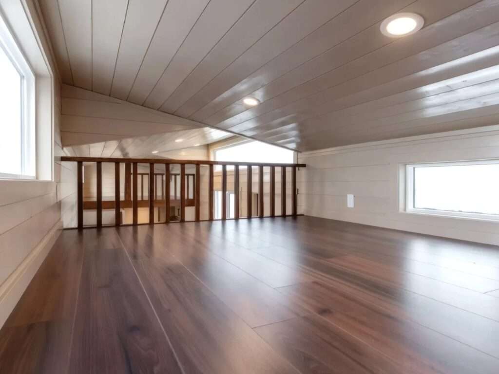 An elevated view from one loft bedroom looking across to the secondary loft area, separated by a wooden safety railing over hardwood floors.