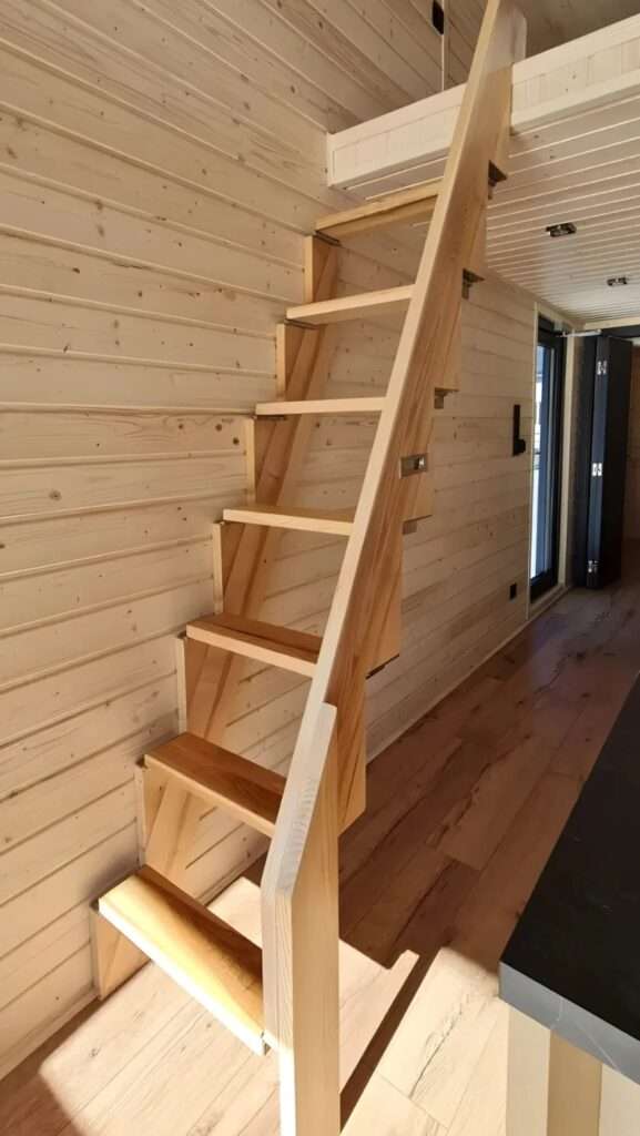 Minimalist wooden staircase leading to the mezzanine in the Samuel tiny house.