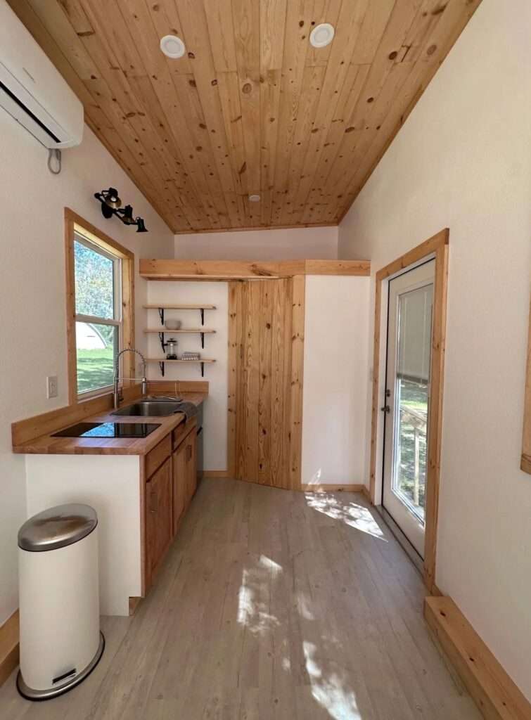 Interior view looking toward the back of the Shanty house, showing wood-planked ceilings, a kitchenette, and an upper storage ledge.