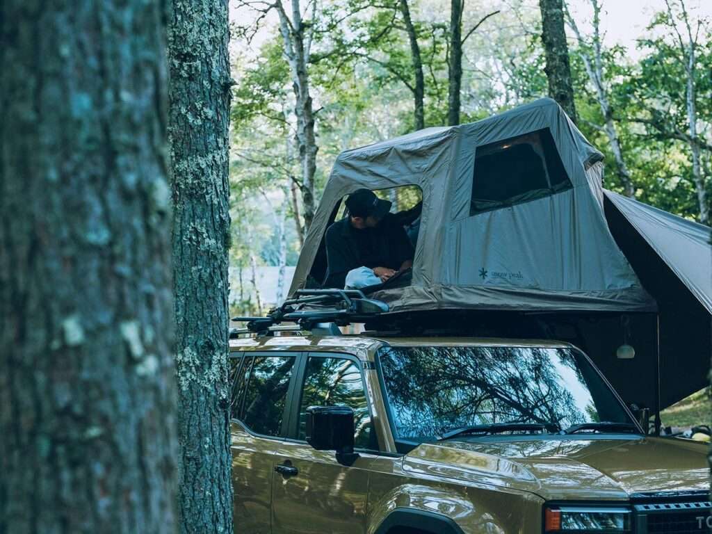 Side view of the rooftop tent among trees, showing large mesh windows for airflow.