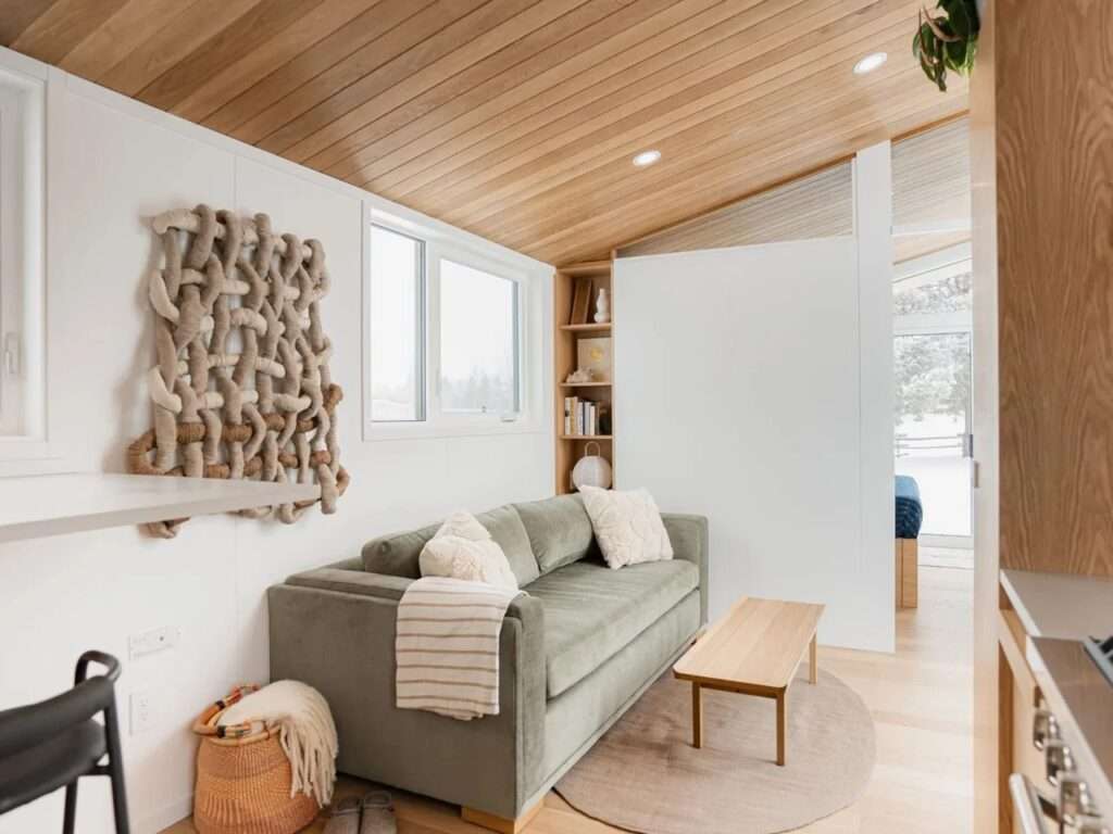 Interior overview of the Halcyon Grand tiny home showing the sloped wood ceiling, green sofa, wood floors, and view looking toward the main bedroom.