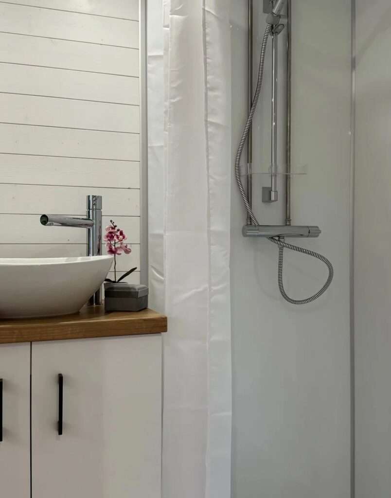 Modern tiny house bathroom with white walls, a chrome shower fixture, and a vessel sink on a wooden vanity.