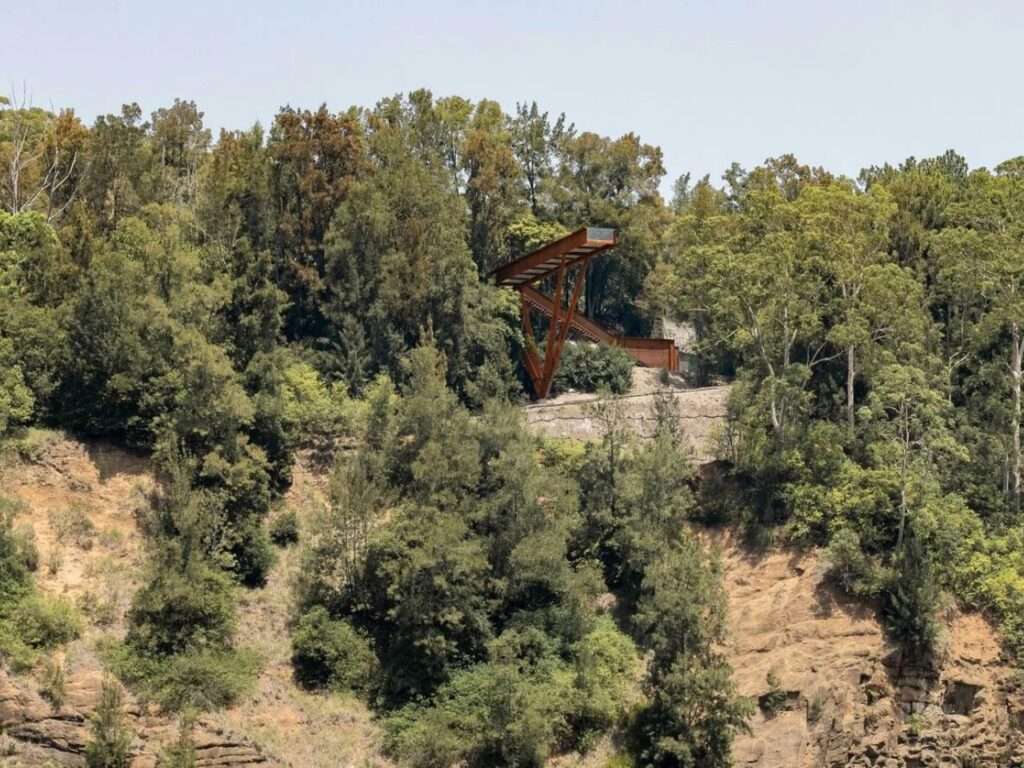 Distant view of the Southern Lookout structure nestled within a thick green forest on a rocky cliff.