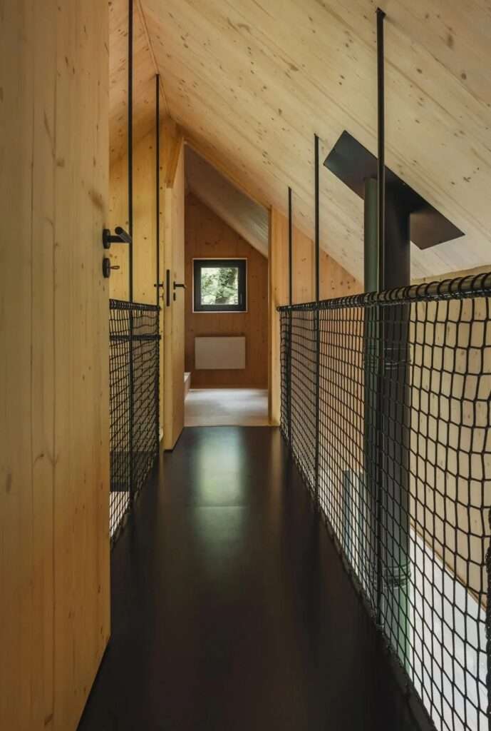 Narrow upper-level hallway in a wooden cabin with black floors and protective mesh railings under a pitched roof.