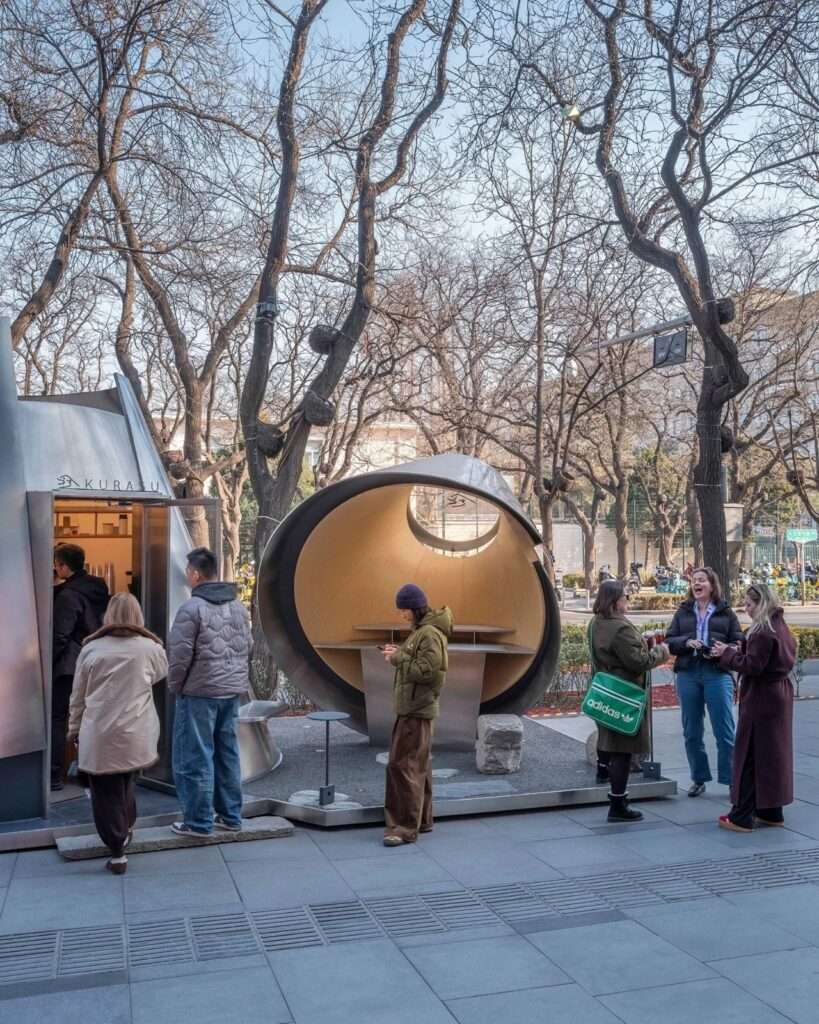 Customers gathering and interacting around the Kurasu coffee pavilion on a public pedestrian walkway in Beijing.