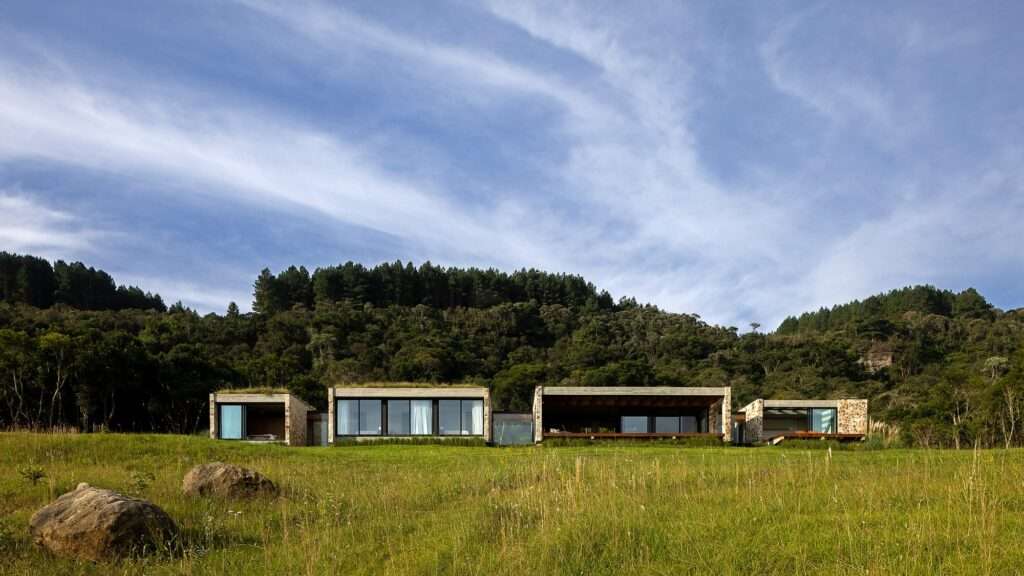 Casa Inter Pires modular pavilions terraced into a steep green hillside slope under a wide cloudy sky.