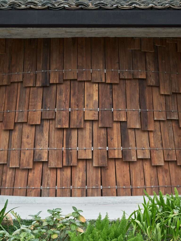 Close-up architectural detail of the Tree Tavern facade showing reclaimed wooden shingles bound by exposed steel cables and tension fixtures beneath an old clay tile roof.