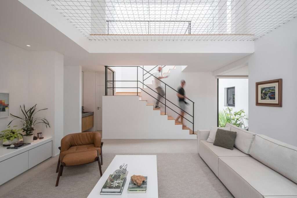 Minimalist wooden staircase with black steel handrails under a double-height ceiling in a modern white living room.