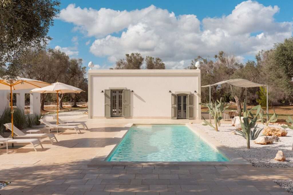 Modern swimming pool at Villa Normanni in Puglia, Italy, featuring white exterior walls, olive trees, and minimalist Mediterranean design.