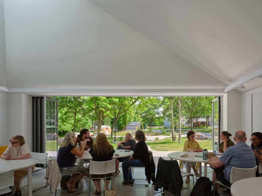 Interior of the pavilion room featuring white walls, a high slanted ceiling with a skylight, and large folding glass doors opening to a green park.