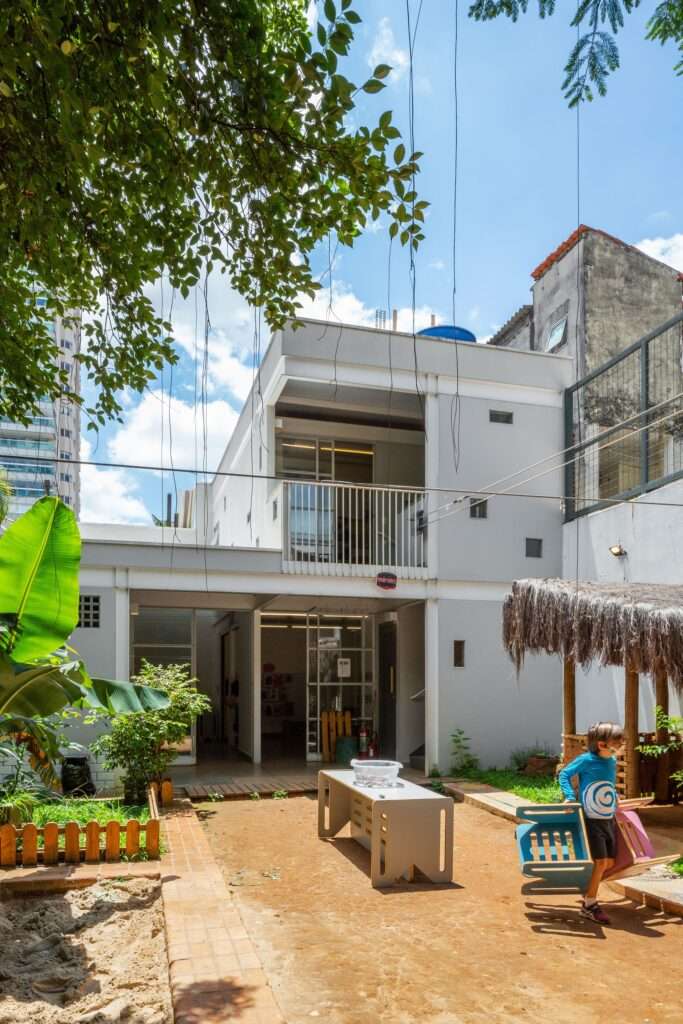 Two-story modern school wing with a balcony overlooking the playground and integrated natural elements.