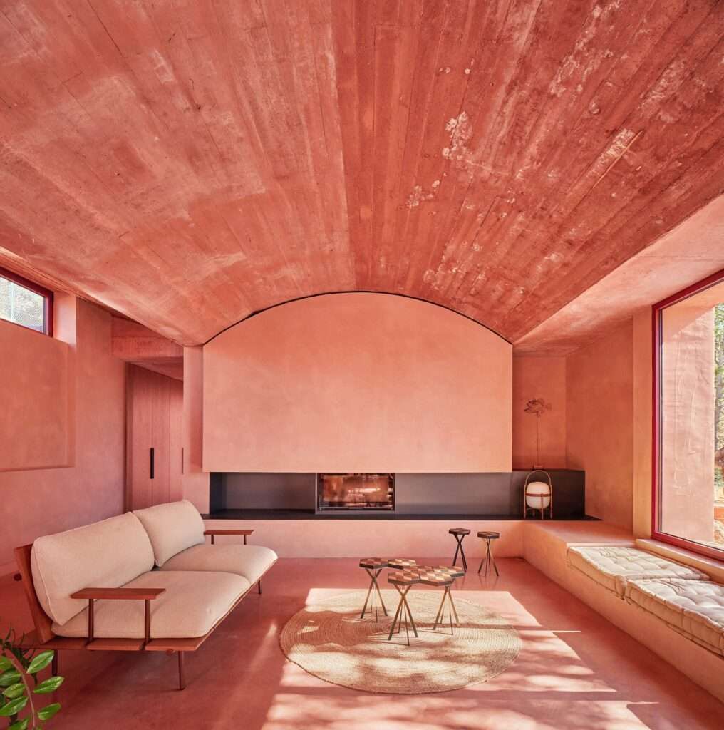 Minimalist living room interior at Casa Sota la Mola featuring a built-in fireplace wall, red concrete flooring, a textured vault ceiling, and a modern sofa.