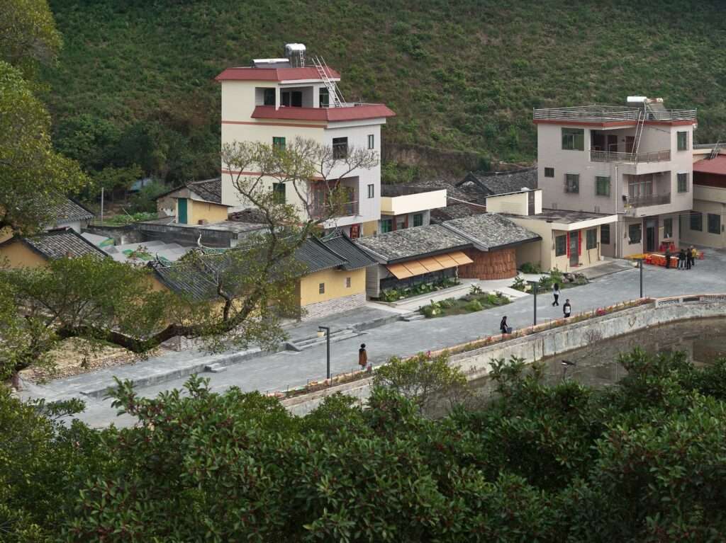High-angle panoramic view of the Tree Village project showing the plaza, the riverfront path, the ancestral buildings, and the surrounding green hills.