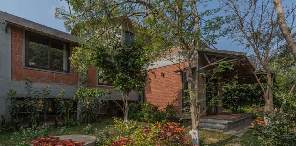 Side view of Svatamman house showing a stilted structural section raised on columns over a green lawn garden with a paved pathway.