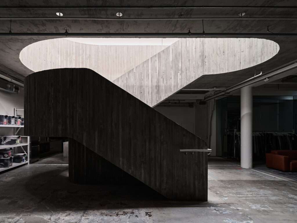 Architectural silhouette of a curved concrete staircase in a dimly lit industrial warehouse conversion for Purple Brand in Vancouver.
