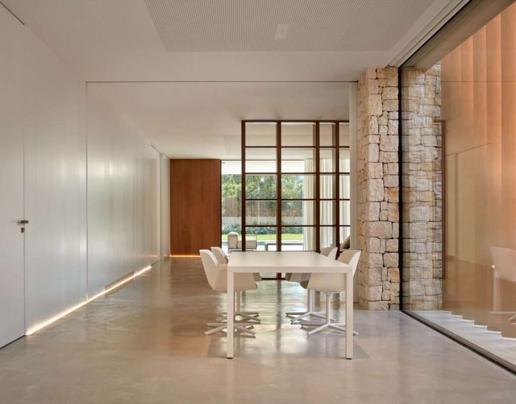 Interior dining space looking toward an outdoor pool area through large sliding glass doors and a stone pillar.