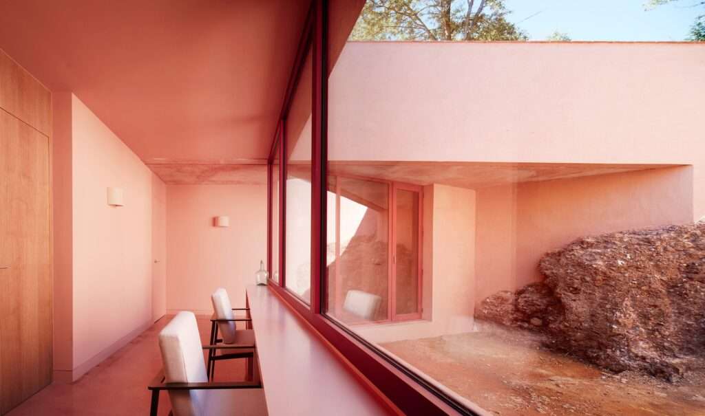 Indoor study desk facing a large window that looks onto an excavated courtyard featuring an exposed natural rock formation embedded in the wall.