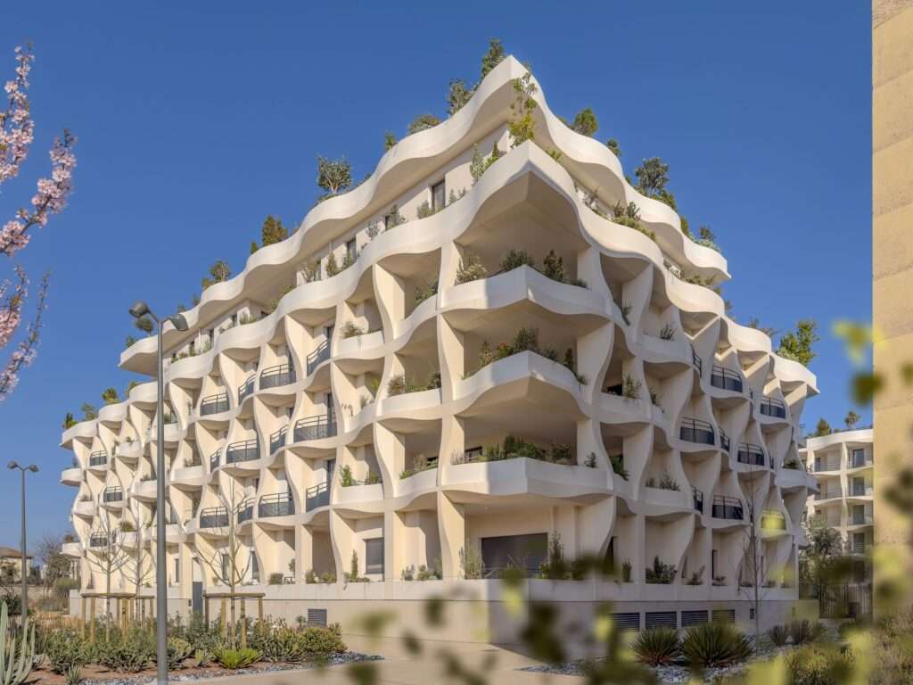 Side view of the Secret Gardens building showing the sculptural white balconies and staggered rooftop terraces with dense vegetation.