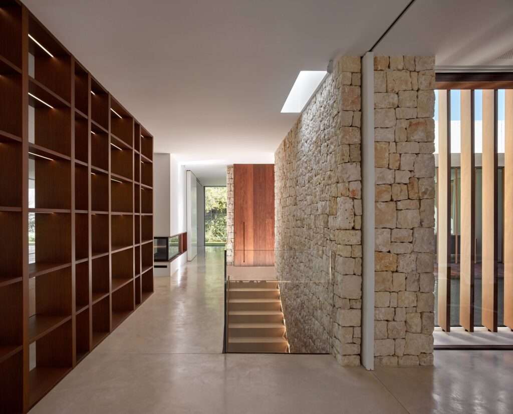 Interior hallway featuring a wooden bookshelf, a stone wall, and a staircase leading to the lower level.