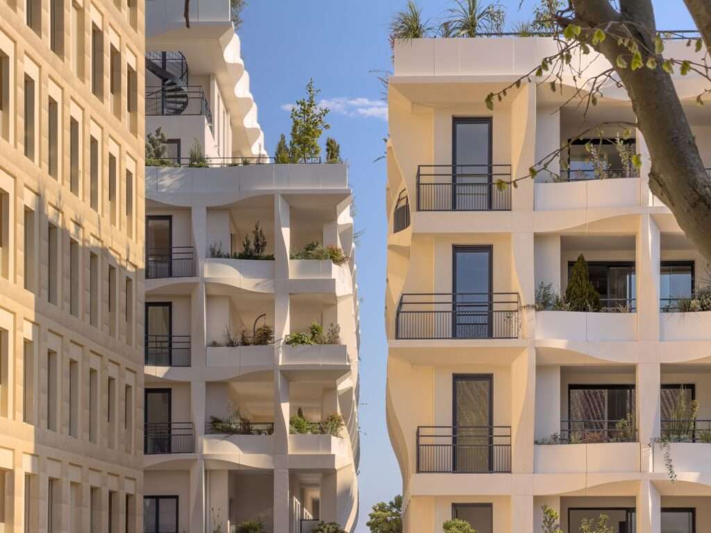 View through an urban gap showing two residential blocks of the Secret Gardens project with integrated greenery and modern facades.
