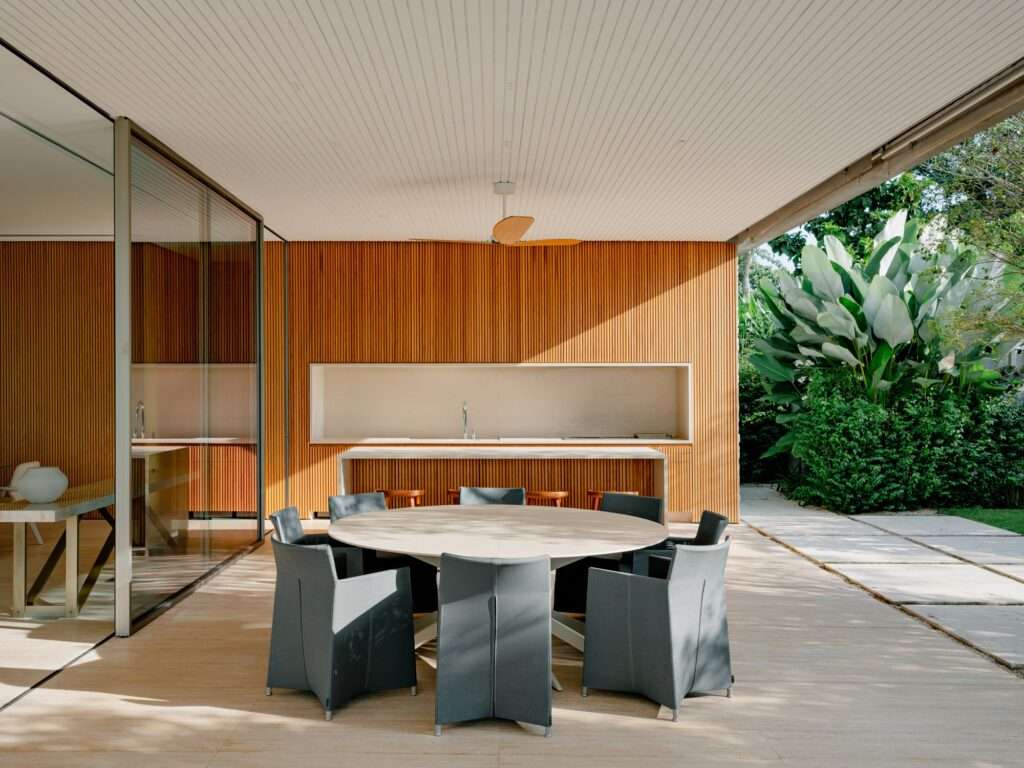 Modern outdoor kitchen and integrated dining patio at Casa Escultura with textured vertical wood panels and minimalist gray chairs.