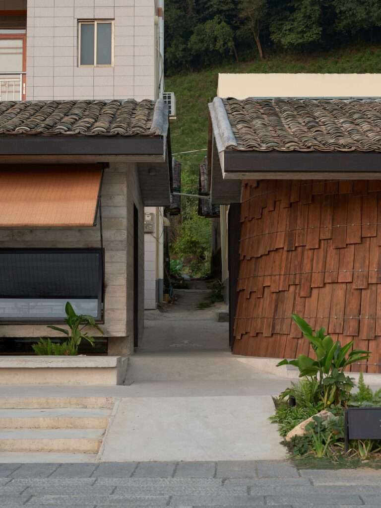 Close-up of the narrow alleyway separating the concrete wall of the teahouse and the curved timber wall of the tavern.