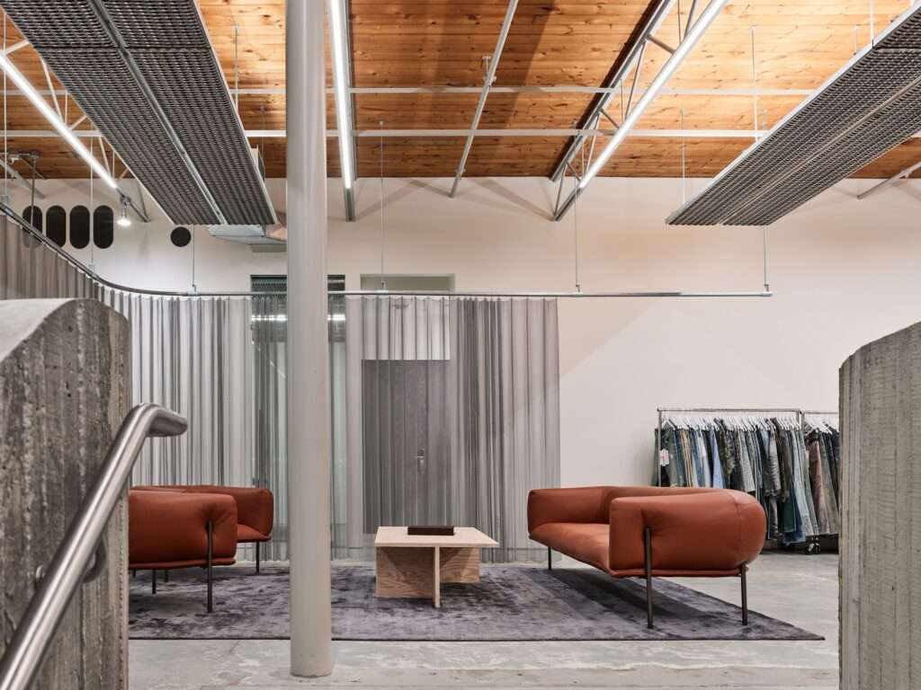 Interior lounge area of Purple Brand Studio with leather sofas, wood plywood furniture, and clothing racks for sample display.